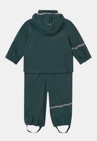 Nepremokavý dáždnik v tmavozelenej farbe s reflexnými pruhmi. Obsahuje elastický kapucňu a manžety, jednopriestranný dizajn a nastaviteľné pätné popruhy.