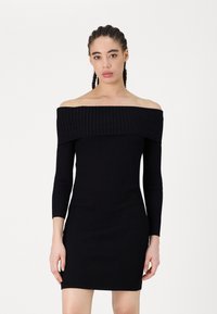 Vestido preto canelado, off-the-shoulder, com mangas longas, silhueta ajustada e tecido texturizado. Acabamento liso e uniforme, sem padrões.