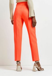 Klarröda skräddarsydda byxor med en smal passform och platt framsida. Tyget har en slät struktur och matchas med vita blockklacksandaler.