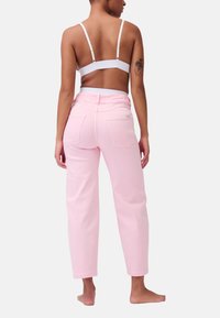 Pantaloni in denim rosa chiaro con vestibilità rilassata, vita alta e tasche posteriori; indossati con un semplice bralette bianco.