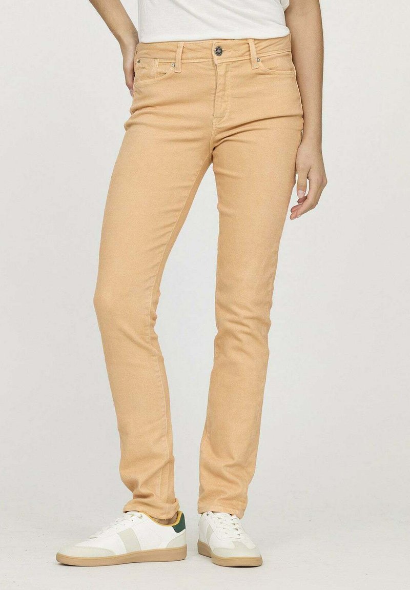 Jean slim beige clair avec cinq poches, une fermeture à bouton et à zip, et des coutures décoratives, associé à des baskets blanches.