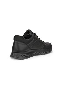 Zapatilla deportiva negra con suela texturizada, cuello acolchado y tejido de malla alrededor del tobillo, vista desde un ángulo lateral trasero.