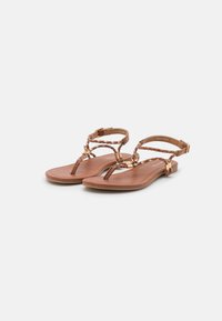 Sandales en cuir marron avec un design de bande tressée, semelle plate et accents métalliques. Brides de cheville ajustables pour un ajustement personnalisé.