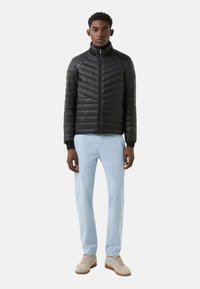 Sort dunjakke med lynlås foran, chevron-syning og opretstående krave, kombineret med lyseblå bukser og beige sneakers.