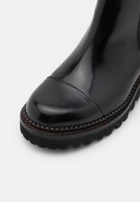 Botte en cuir noir avec bout arrondi, coutures visibles et semelle épaisse et robuste avec des crampons profonds pour une bonne adhérence.