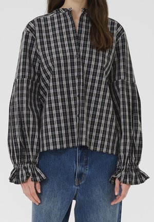Woman wearing a black and white plaid button-up blouse with ruffled cuffs and blue jeans, shown from the neck to mid-thigh.