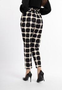 Zwart en beige geruite broek met een elastische tailleband, taps toelopende benen en een gladde textuur, gecombineerd met zwarte hoge hakken.