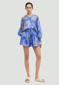 Plava, lagana, uzorkovana košulja s gumbima i kratke hlače s elastičnom trakom. Tkanina ima mekanu teksturu i suptilan sjaj.