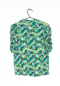 Zielona bluzka w kwiaty z krótkimi bufkami. Charakteryzuje się mieszanką zielonych, fioletowych i żółtych wzorów kwiatowych na jasnym tle.