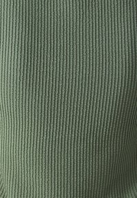 Ribbed sweater in muted green, made of soft fabric. The texture features vertical stripes, creating a tactile pattern across the surface.