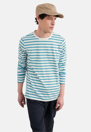 Maglietta a maniche lunghe a righe blu e bianche con collo rotondo, abbinata a pantaloni scuri e un cappellino beige chiaro.
