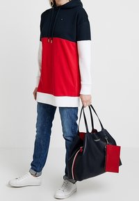 Bluza z kapturem w kolorze granatowym, czerwonym i białym, w połączeniu z niebieskimi dżinsami oraz dużą granatową torbą na ramię z czerwonymi akcentami.