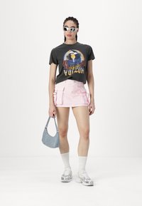 Camiseta gráfica gris con estampado colorido, mini falda rosa con bolsillos, bolso de mano azul claro, calcetines blancos y zapatillas plateadas.
