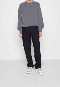 Sudadera gris con cuello redondo y mangas raglán, combinada con pantalones azul marino y zapatillas grises con acentos blancos.