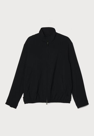 Chaqueta negra con cremallera, cuenta con un alto cuello, cintura elástica, tejido texturizado y dos bolsillos laterales. Acabado suave con un corte holgado.