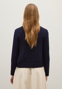Maglione lavorato a maglia blu marino con polsini e orlo a coste, caratterizzato da un motivo testurizzato e un design aderente. Vista posteriore, capelli lunghi visibili.