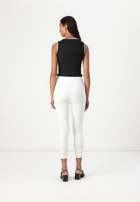 Top negro sin mangas con acentos blancos bordados, combinado con pantalones ajustados blancos y sandalias de tacón cuadrado negras. Vista trasera del conjunto.