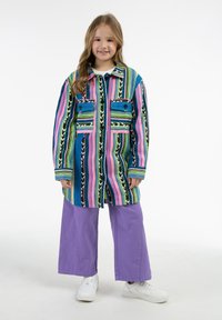 Pestrý pruhovaný kabát s dvoma prednými vreckami, so zapínaním na gombíky a golierom, skombinovaný so širokými levanduľovými nohavicami a bielymi teniskami.