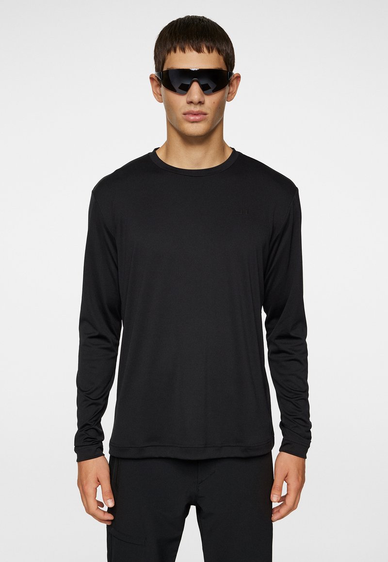 Svart långärmad skjorta i slätt tyg, med rundad halsringning och minimalistisk design. Bärs med eleganta svarta solglasögon.