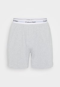 Graue Baumwoll-Boxershorts mit einem elastischen Bund, der ein weißes Band mit der Aufschrift "Calvin Klein" in Schwarz trägt. Glatte Textur, lässige Passform.