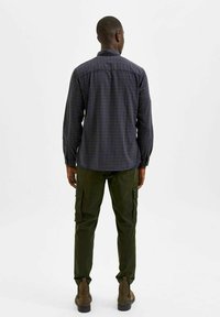 Camicia a maniche lunghe con motivo a quadri blu navy, abbinata a pantaloni cargo verde oliva. Tessuto morbido e vestibilità casual con cucitura sulla spalla posteriore.