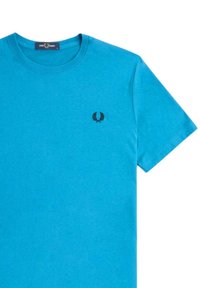 Camiseta de algodón azul de manga corta, con cuello redondo y logotipo bordado en negro en el lado izquierdo del pecho. Textura suave, diseño casual.