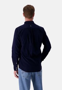 Camicia button-up in corda blu navy con maniche lunghe, caratterizzata da un piccolo logo sopra il colletto e bottoni argentati sui polsini.