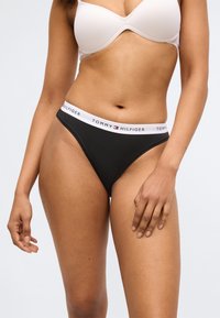 Perizoma nero con una fascia in vita bianca con il nome del marchio "TOMMY HILFIGER." Il materiale sembra morbido con una consistenza liscia.