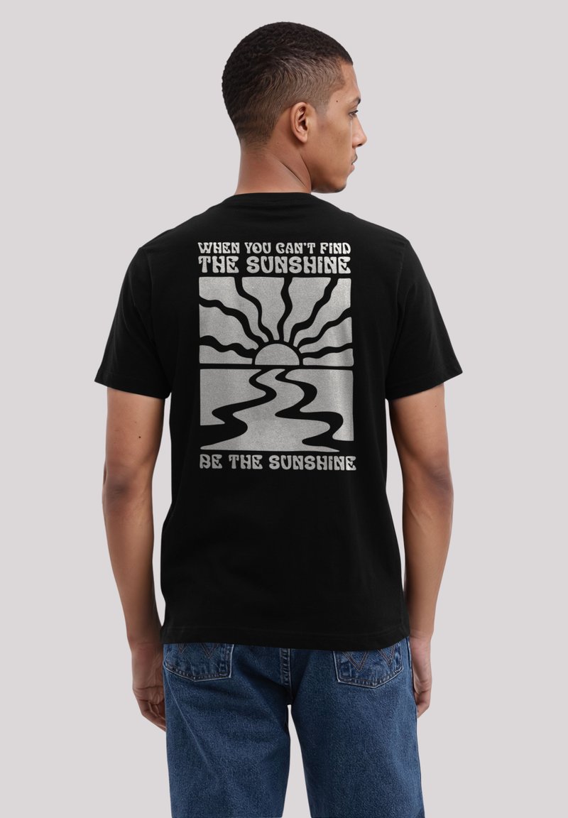 Schwarzes Baumwoll-T-Shirt mit einem silbernen Grafikdesign von Sonne und Wellen, mit Text in fetter weißer Schrift auf der Rückseite.