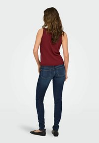 Haut sans manches bordeaux associé à un jean bleu foncé ajusté. Le haut présente un col côtelé, tandis que le jean a un design classique à cinq poches.