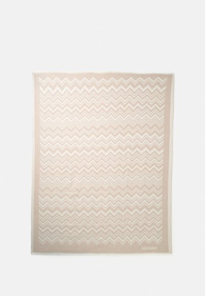 Tissu rectangulaire beige avec motif chevron en zigzag blanc et bordure unie, logo « MISSONI » en bas à droite.