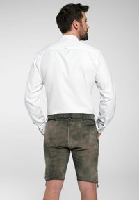 Wit overhemd met lange mouwen en knoopmanchetten, gecombineerd met groenbruin shorts met zijzakken en decoratieve knopen aan de zijkanten.