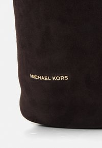 Juodas zomšinis krepšys su lygiu paviršiumi ir auksiniu "MICHAEL KORS" logotipo akcentu, suapvalintos formos dizainu.