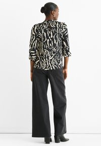 Black and beige patterned blouse with three-quarter sleeves, keyhole back detail, paired with high-waisted wide-leg black jeans and black block heels.