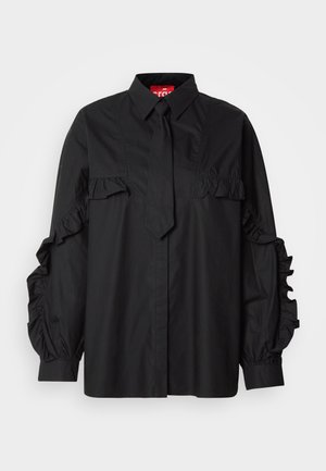 Čierna košeľa s volánovými detailmi na rukávoch, s gombíkovou légou a viazačkou na golieri. Vyrobená z hladkej, ľahkej látky.