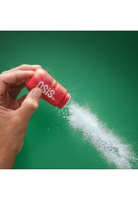 Bouteille rouge d'OSIS+ poudre tenue au-dessus d'un fond vert, distribuant une poudre blanche en éventail, mettant en valeur sa forme ronde et son étiquette bien visible.