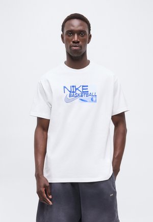 Bărbat purtând un tricou alb Nike Basketball și pantaloni scurți gri închis, stând în fața unui fundal alb simplu.