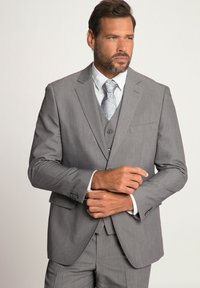 Completo grigio a tre pezzi con finitura texture, dotato di giacca a due bottoni, rever a punta e panciotto abbinato. Camicia bianca e cravatta a fantasia.