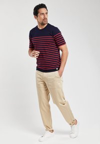 Marine-stribet t-shirt med røde vandrette linjer, parret med lyse beige bukser og hvide sneakers. Casual, afslappet pasform.