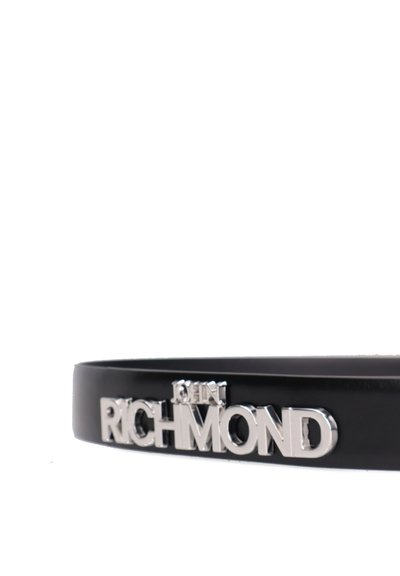 Ceinture noire avec des lettres métalliques argentées formant le mot "RICHMOND" et un petit "JHN" au-dessus du "H" sur un fond blanc.