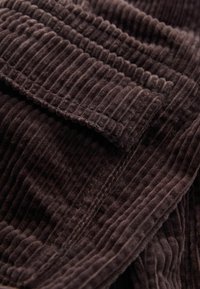 Gros plan d'un tissu en velours côtelé marron montrant des rainures verticales texturées et des couches pliées.