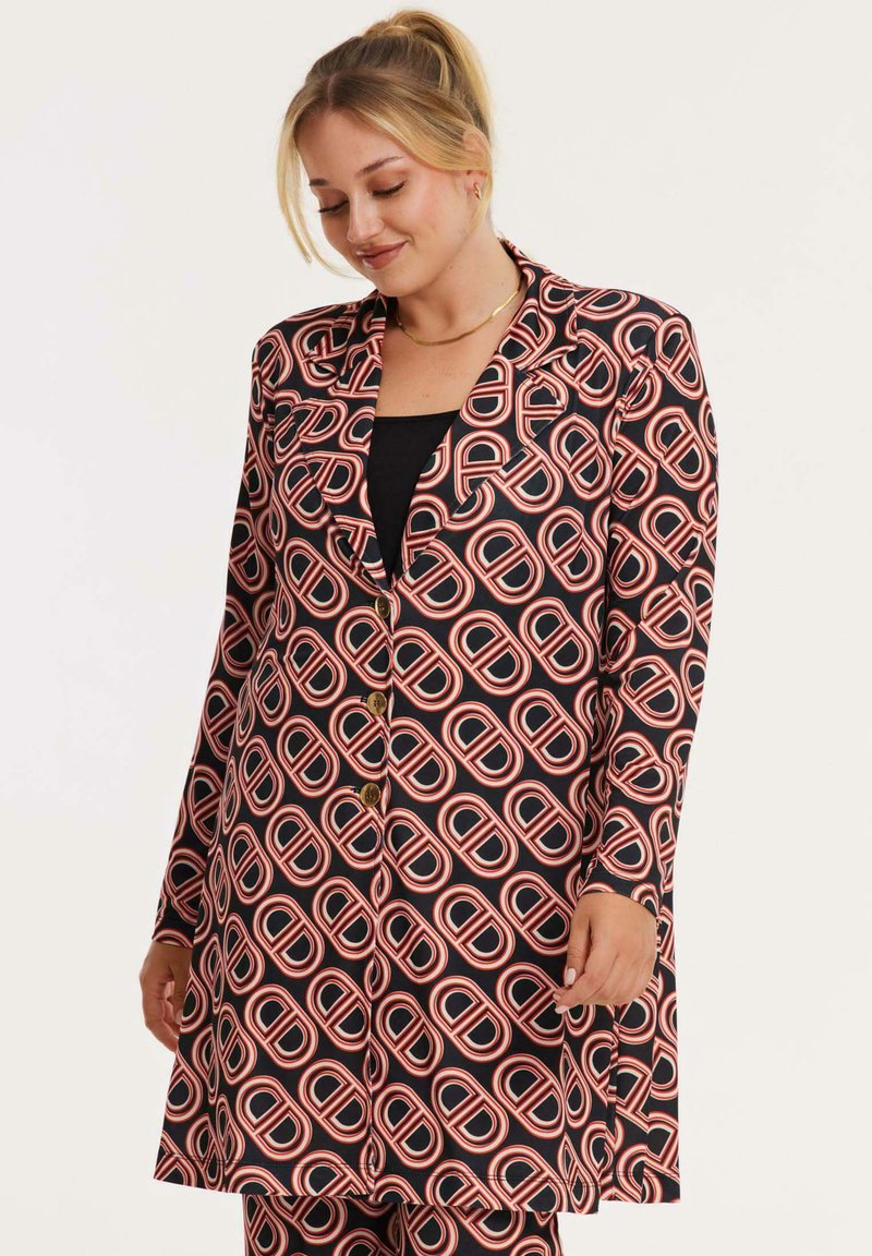 Zwarte blazer met een herhalend rood en wit cirkelpatroon, voorzien van een notched lapel, knoopsluiting en lange mouwen. Gladde textuur.