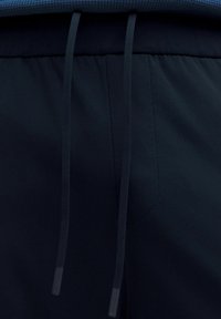 Primer plano de la cinturilla de unos pantalones de chándal azul marino con cordones y detalles de costura visibles.