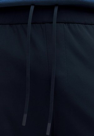 Close-up van de tailleband van donkerblauwe sweatpants met trekkoorden en zichtbare stikseldetails.
