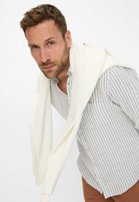 Men's button-down shirt with gray and white stripes, paired with a cream-colored sweater draped over the shoulders, and brown pants.