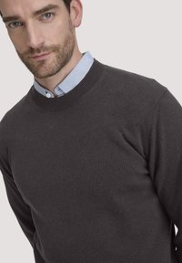 Donkergrijs sweater met een geribbelde ronde hals, gemaakt van gladde, zachte stof. Gelaagd over een lichtblauw overhemd met kraag.