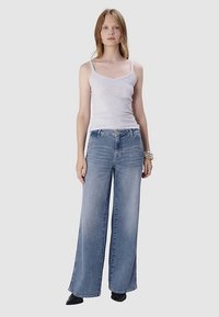 Jasnoszary dopasowany top na ramiączkach w zestawie z szerokimi, wyblakłymi niebieskimi dżinsami. Dżinsy mają średni stan i prosty krój.