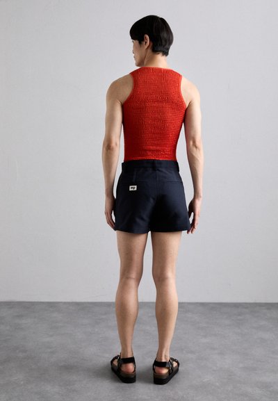 Punainen raidoitettu tanktoppi yhdistettynä tummansinsisiin shortseihin, joissa on kaksi takataskua, litteä vyötärö ja mustat nilkkaketjut.