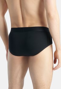Des slips noirs pour hommes avec un tissu lisse, une taille élastique et des rayures latérales discrètes. Le design est ajusté et minimaliste.