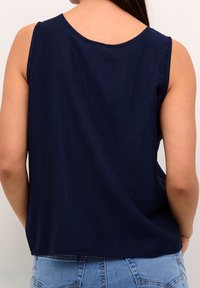 Ärmlös marinblå topp med rund halsringning och ett flödande snitt. Materialet verkar texturerat, med en slät yta och lös passform.